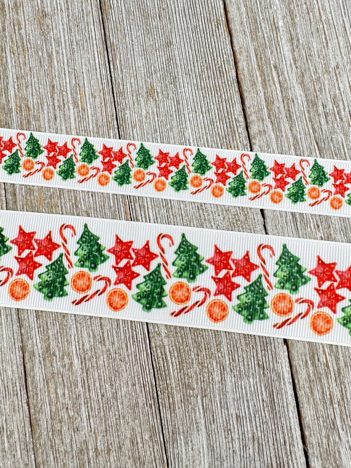 May include: White ribbon with a repeating Christmas pattern. The pattern includes red stars, green Christmas trees, orange slices, and red and white candy canes. The ribbon is displayed on a wooden surface.