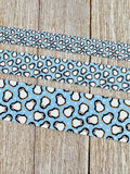 May include: Three ribbons with a penguin pattern on a light blue background. The top ribbon has small penguins, the middle ribbon has medium-sized penguins, and the bottom ribbon has large penguins. The penguins are white with black details and orange beaks.